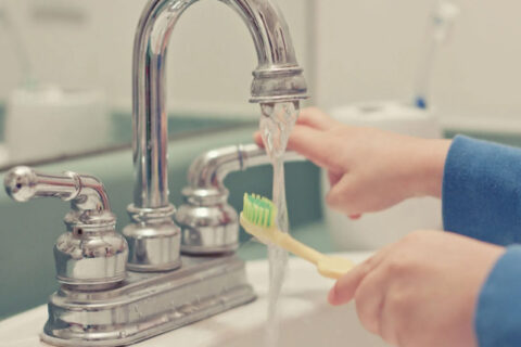 cleaning toothbrush under tap water